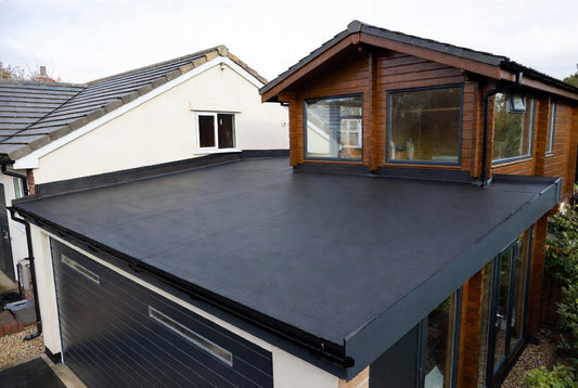 Seamless black EPDM rubber flat roof installed on a UK garage and attached timber log cabin, showing the smooth single-sheet membrane and neat edge trims